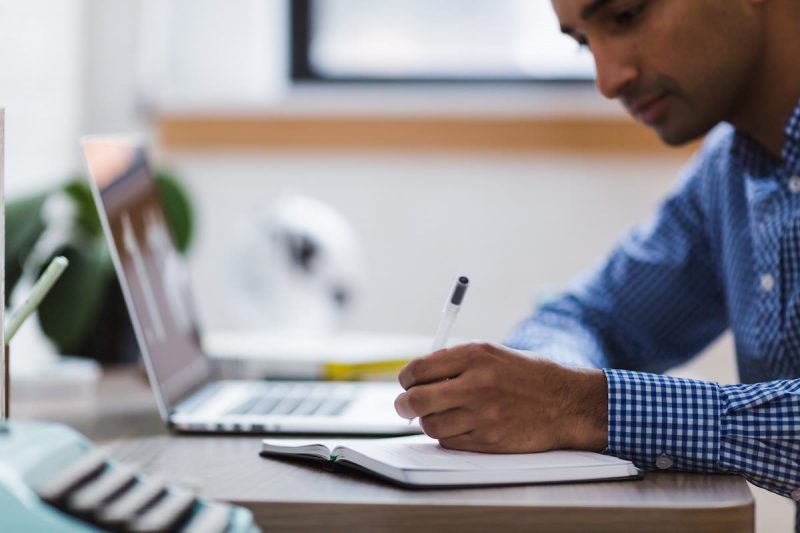 man met pen en papier achter een laptop